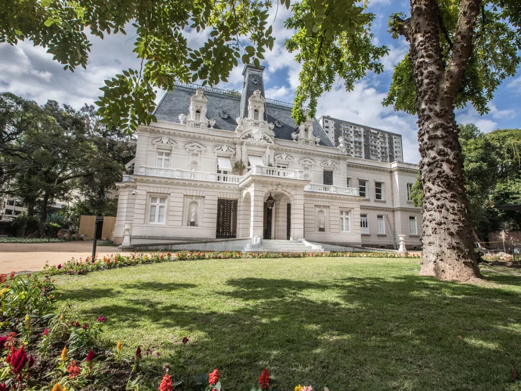 foto mostra a arquitetura da casa firjan ao fundo e no primeiro plano uma área gramada